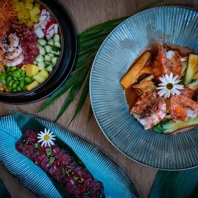 Dreiteilige Food-Komposition aus Poké Bowl, Lachsgericht und Longplate mit Thunfischtatar – kunstvoll angerichtet auf tropischem Hintergrund.