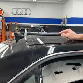 A black Audi car is undergoing paintless dent repair on its roof, with tools and a hand visible working on the surface.