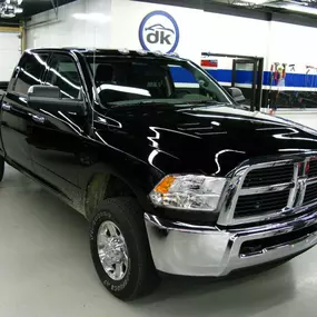 A shiny black Ram 2500 pickup truck with chrome accents is parked inside a clean, well-lit auto detailing or repair shop.