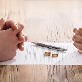 Two individuals sit across from each other at Ibrahim & Dobaria Law, PLLC, with hands clasped over a divorce agreement, symbolizing a mutual legal separation and representation in family law.