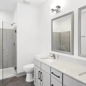 A modern bathroom with a walk-in shower, toilet, and double sinks.