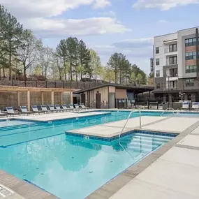 A large outdoor swimming pool with lounge chairs and a building in the background.