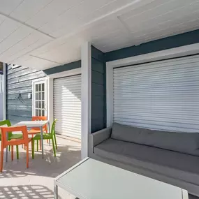 A grey couch is on a patio with a table and chairs.