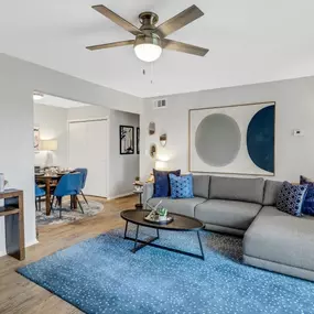 A living room with a grey couch, a blue rug, and a ceiling fan.
