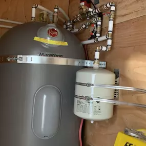 High-efficiency Rheem Marathon water heater installed with precision PEX connections and pressure tank in a utility closet.