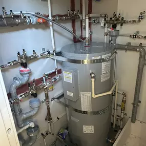 A complex hot water plumbing system in a commercial or multi-unit residential setting, featuring a well-organized network of pipes and safety components.