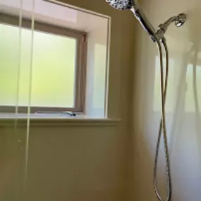 A sleek chrome handheld showerhead installed near a frosted window, part of a clean and modern bathroom upgrade.