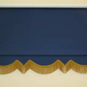 Blue roller shade with scalloped gold fringe trim along the bottom edge