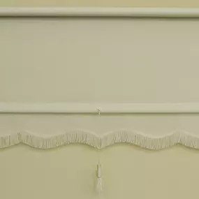 Off-white roller shade with scalloped fringe trim and decorative hanging tassel