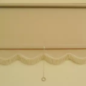 Beige roller shade with scalloped fringe trim and a ring pull cord