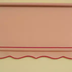 Pink roller shade with scalloped bottom edge and red trim accent