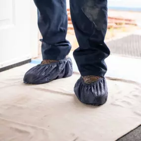 Close-up of a technician’s boots covered in protective shoe covers, standing on a cloth to protect a customer’s floor.