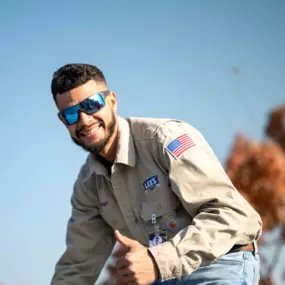 A cheerful Lee’s Air technician in uniform gives a thumbs up while working outdoors.
