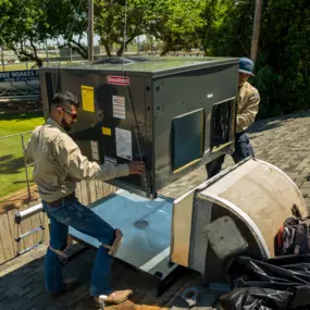 Two Lee’s technicians install an HVAC unit on a rooftop using a crane