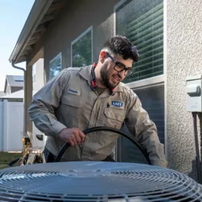 A technician labeled “Orlando” services an outdoor air conditioning unit using a hose to clean an hvac condenser unit.