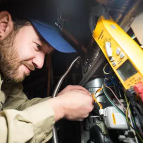 A Lee’s Air technician is performing intricate wiring inside an HVAC system with a multimeter in view.