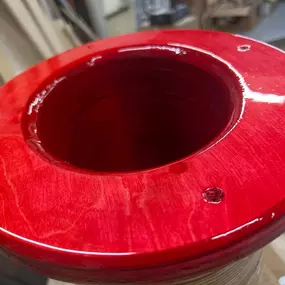 This close-up captures a bright red, glossy circular object with a central hole, revealing visible wood grain beneath the translucent finish. It appears to be a finished component of a larger structure.