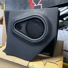 A black, custom-built car speaker enclosure with a large central speaker and a smaller tweeter is prominently displayed. The textured surface of the enclosure suggests a durable, high-quality audio component.