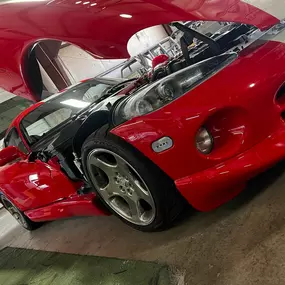 A sleek, red sports car with white stripes has its hood, doors, and trunk open, revealing its engine and interior details. The car is parked indoors, possibly in a garage or showroom, under bright lighting.