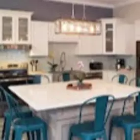 Spacious kitchen with white cabinets, teal chairs around a large island, modern light fixture, stainless steel appliances, creating a cozy, inviting feel.