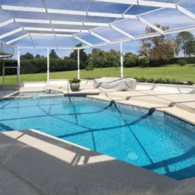 Outdoor pool with a white screened enclosure featuring a clear blue sky. The poolside area is spacious and surrounded by lush green grass.