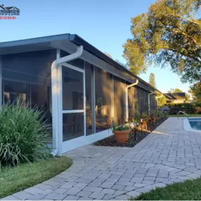 House with screen room. The front yard has plants and trees.