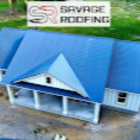 High-angle, full shot of a house under construction. The house has a light beige or cream-colored exterior, and a vibrant, deep blue metal roof with a noticeable pattern or texture.