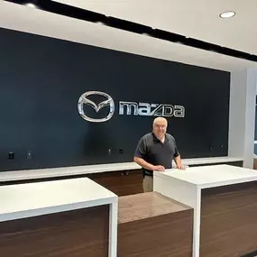Whaling City Mazda representative standing behind the front desk with the Mazda logo in the background.