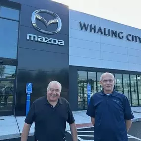 Whaling City Mazda representatives smiling in front of the front entrance with the Whaling City Mazda branding.