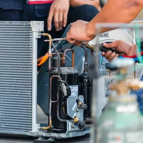 An HVAC technician is actively working on an outdoor air conditioning unit, using specialized tools to inspect and repair the system. Dressed in uniform and safety gear, the technician is focused on ensuring the unit runs efficiently and safely. This image highlights the importance of professional A/C repair, seasonal maintenance, and expert diagnostics to prevent breakdowns and extend equipment life. Perfect for illustrating residential or commercial HVAC service in action.
