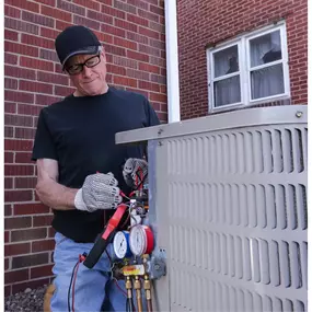 An HVAC technician is servicing an air conditioning unit outdoors, using diagnostic tools to check refrigerant levels and ensure the system is running efficiently. Dressed in uniform with safety gear, the technician demonstrates the importance of professional A/C repair, seasonal maintenance, and proper system care. This image reflects expert service, reliable cooling solutions, and the value of regular HVAC inspections to prevent breakdowns and maintain indoor comfort.