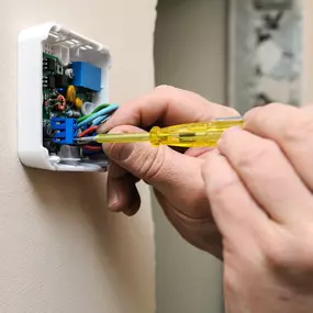 An HVAC technician is shown adjusting or replacing a wall-mounted thermostat inside a home or business. Using specialized tools, the technician ensures accurate temperature control and proper connection to the heating and cooling system. This image represents professional HVAC service, thermostat troubleshooting, and smart thermostat upgrades for improved energy efficiency and comfort. Perfect for promoting residential or commercial HVAC system diagnostics and climate control solutions.