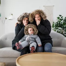 A family sits bundled up on a couch under blankets, visibly cold and uncomfortable inside their home. Parents and children are layered in sweaters and using hot drinks or space heaters to stay warm—signs of a failing or inefficient heating system. This image highlights the need for reliable home heating, emergency HVAC repair, and seasonal furnace maintenance. Ideal for promoting residential heating services, energy-efficient upgrades, or preventive maintenance plans.