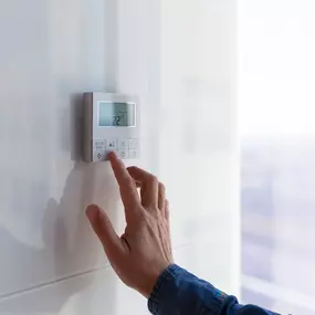 A close-up of a hand adjusting the temperature on a digital or smart thermostat, controlling the indoor climate for optimal comfort. The display shows a temperature change, symbolizing seasonal transitions, energy efficiency, and homeowner control over their heating and cooling system. This image is perfect for promoting thermostat upgrades, smart HVAC controls, and the importance of regular system maintenance to maintain year-round comfort and reduce energy costs.