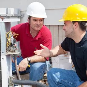 Two HVAC technicians work together on an outdoor air conditioning unit, performing diagnostics, checking refrigerant levels, and ensuring proper system performance. Dressed in uniform and using professional tools, the team collaborates to complete the job efficiently and accurately. This image highlights expert service, teamwork, and the importance of routine A/C maintenance and repair for reliable home or commercial cooling.