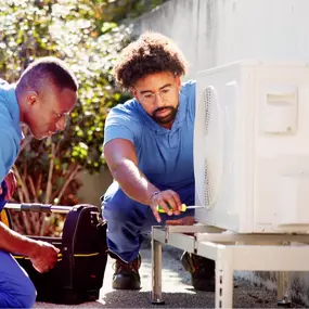 Two HVAC technicians are servicing a small outdoor air conditioning unit, using diagnostic tools and working together to ensure the system is running efficiently. The compact A/C unit is ideal for a smaller home, apartment, or office space, and the technicians’ teamwork highlights the importance of professional maintenance, precise installation, and reliable repair. This image reflects expert care, system optimization, and efficient cooling for compact spaces.