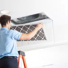An HVAC technician wearing a uniform and gloves is shown changing an air filter in a residential heating and cooling system. The technician carefully slides out the old, dirty filter and replaces it with a clean one, helping to improve airflow, reduce energy costs, and maintain indoor air quality. This image illustrates the importance of regular HVAC maintenance, including air filter replacement, to keep systems running efficiently and prevent costly repairs. Ideal for use in preventive maintena