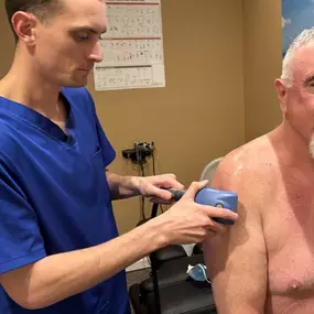 Dr. Gage Kirstein performing shockwave therapy on a patient's shoulder