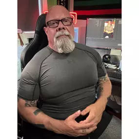 In this photo, Connor MacIvor—widely recognized as “Connor with Honor”—sits confidently in his home studio. Wearing a fitted athletic shirt that reflects his dramatic weight-loss and fitness transformation, Connor showcases the discipline and strength that define both his personal journey and professional approach. Behind him, dual computer screens display his content creation setup, emphasizing his role as a leading voice in Santa Clarita real estate and AI-powered automation systems. Tattoos o