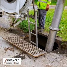 An Advanced Plumbing & Drain technician is performing a storm drain or sewer line cleaning using vacuum equipment, with the manhole grate lifted and access setup visible.