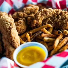 A basket of crispy chicken tenders served with fries and dipping sauce.