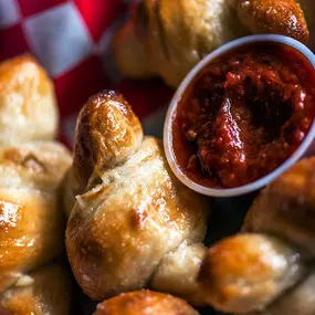 Freshly baked garlic knots served with a side of marinara dipping sauce.