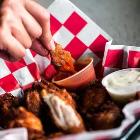 Crispy fried chicken wings served with buffalo and ranch dipping sauces in a checkered basket.