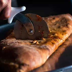 Golden brown calzone fresh out of the oven, sliced open to reveal melted cheese and savory fillings. Served hot on a pan and cut fresh with a pizza cutter.