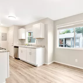 A kitchen with white cabinets and a window overlooking a house.