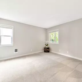 A room with a carpeted floor and two windows.
