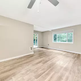 A room with a ceiling fan and light, hardwood floors, and a window with a view of trees.