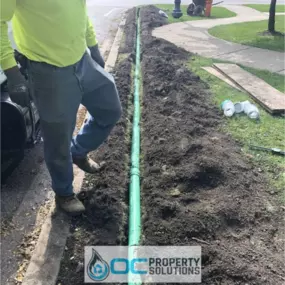 A crew member stands beside a freshly installed green sewer or drainage pipe during a residential utility line replacement project.