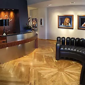 The image captures the stylish interior of Skin Spa Soho, featuring a modern reception desk, a unique black leather sofa, and striking parquet wood flooring. Framed portraits add a personal touch to the chic and welcoming space.