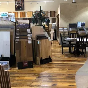 This image shows a flooring showroom with diverse wood flooring samples, including large upright displays and installed sections. The lighting highlights the various textures and tones available for customers.